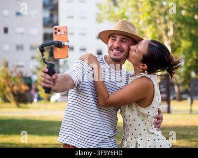 Giovane uomo e donna che condividono un momento romantico mentre si filmano con un telefono cellulare montato su uno stabilizzatore portatile. Foto Stock