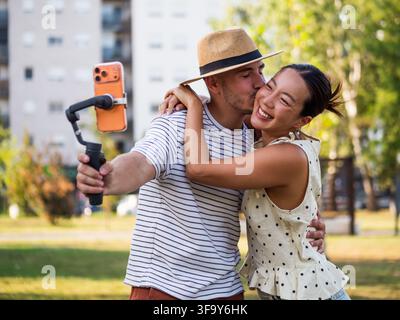 Giovane uomo e donna che condividono un momento romantico mentre si filmano con un telefono cellulare montato su uno stabilizzatore portatile. Foto Stock