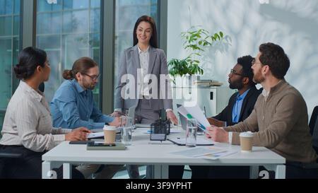 Donna d'affari caucasica, capo, in piedi mentre parla con colleghi di una squadra commerciale di successo durante una riunione in ufficio. Donna leader parla con manager e colleghi Foto Stock