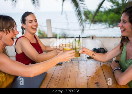 Gruppo di giovani donne felici trentenni che brindano con cocktail su una terrazza all'aperto sorridendo, stile di vita digital nomad Foto Stock