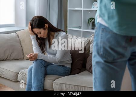Donna arrabbiata seduta sul divano durante un conflitto con un uomo in piedi nelle vicinanze Foto Stock