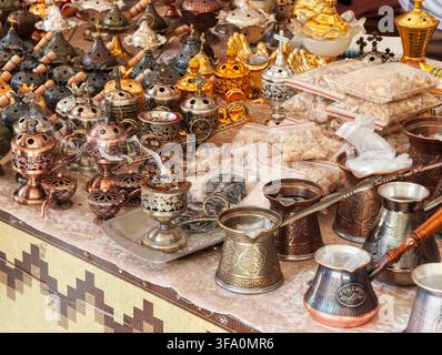Caffettiere, teiere e incensieri tradizionali in rame e ottone su un banco del mercato. Articoli in metallo ornati con motivi intricati e superfici riflettenti Foto Stock
