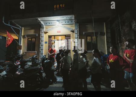 Hanoi, Vietnam, 1 settembre 2025: Vicini che si riuniscono all'ingresso di una casa in un vicolo di Hanoi di notte Foto Stock