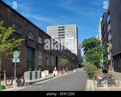 Vista stradale di Oostenburg Amsterdam con magazzino industriale storico in mattoni convertito, contenitori per il riciclo, biciclette e grattacieli moderni Foto Stock