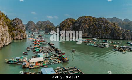 Vista aerea di un villaggio di pescatori galleggiante e piattaforme di acquacoltura su acque smeraldine, circondato da drammatiche isole di calcare nella baia di Lan Ha, Hai Phong Foto Stock