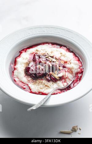 Tradizionale budino di riso danese risalamande servito in una ciotola bianca, guarnito con salsa di ciliegie dolce, ciliegie intere, mandorle tritate e una spolverata di c Foto Stock