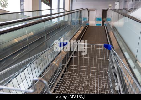 Un carrello della spesa è posizionato alla base di una passerella mobile e di una scala mobile vuote in un edificio commerciale moderno Foto Stock