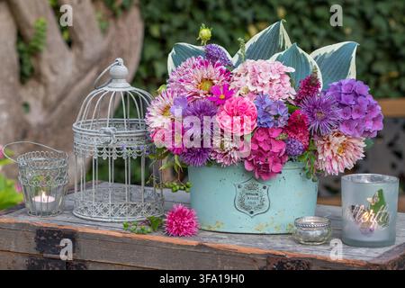 Composizione floreale di dalie, aster cinesi, rosa, fiori di ortensia, fiori di cespuglio farfalla e foglie di hosta, lanterne da tavolo e gabbia per uccelli Foto Stock