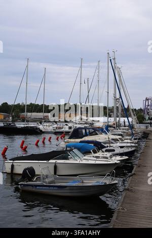Piccole barche ormeggiate lungo il molo di Skeppsholmen a Stoccolma, Svezia, con il lungomare e le acque calme nelle vicinanze. Foto Stock