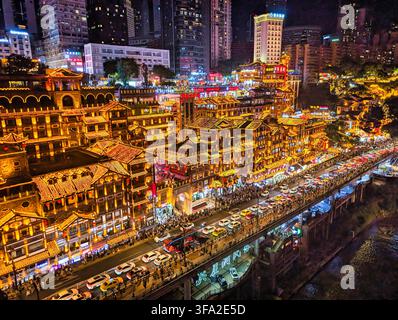 Vista dell'architettura su palafitte illuminata della grotta di Hongya con traffico intenso sul ponte e lo skyline urbano di notte a Chongqing, Chongqing, Cina. Foto Stock