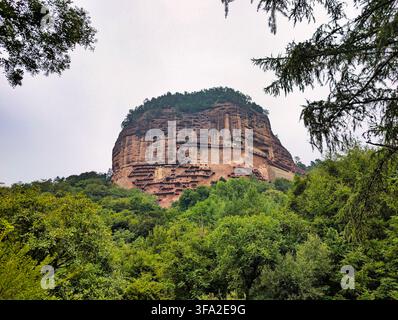 Vista delle grotte storiche di Maijishan scavate nella ripida parete montana, circondate da una lussureggiante foresta verde e alberi a Tianshui, in Cina. Foto Stock