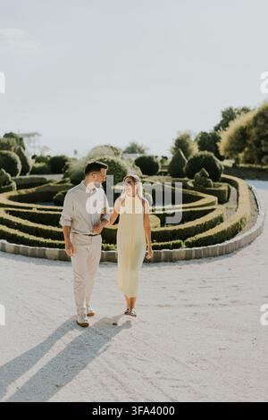 Una coppia si gode una bella passeggiata in un giardino pittoresco pieno di vegetazione vivace e luce calda, condividendo sorrisi e risate insieme. Foto Stock
