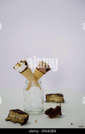 Coni di gelato al cioccolato e alla vaniglia con pezzi di torta al cioccolato intorno Foto Stock