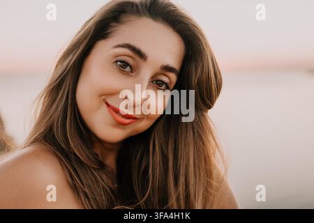 Ritratto di donna sulla spiaggia con una giovane bruna sorridente dai capelli lunghi che gode di un tramonto splendido in riva al mare durante l'ora dorata Foto Stock