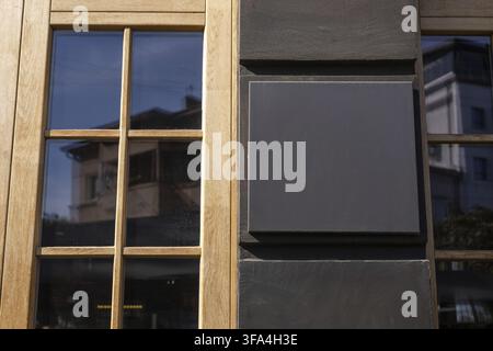Un cartello nero in lavagna vuoto è esposto sulla parete esterna di un ristorante, illuminato dalla calda luce del pomeriggio. Modello urbano per le aziende Foto Stock