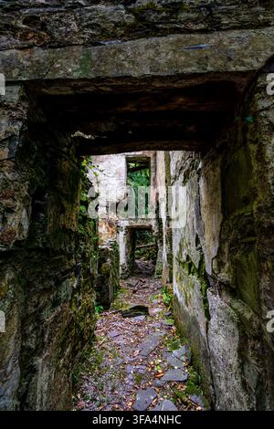 Corridoio stretto che si affaccia su porte in pietra consecutive all'interno di un cottage senza tetto abbandonato, circondato da edera e macerie di ardesia a Dorothea Quarry Foto Stock