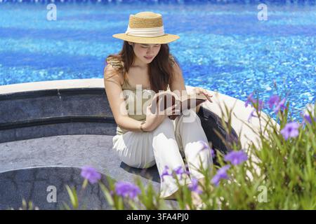 Vacanze estive giovane donna asiatica che legge un libro rilassante in piscina Foto Stock