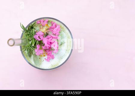 Vista dall'alto di una bevanda al matcha con fiori e rosmarino su rosa Foto Stock