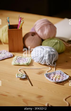 Palle di lana colorate e uncini per uncinetto sul tavolo in un laboratorio di maglia Foto Stock