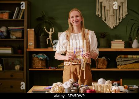 Ritratto di una donna sorridente che tiene un telaio in un laboratorio di maglia Foto Stock