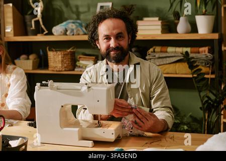 Ritratto di un uomo sorridente che usa una macchina da cucire in un laboratorio creativo Foto Stock