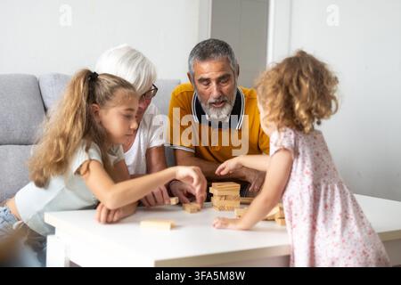 Nonni felici che giocano a torre di blocchi di legno con le loro nipoti a casa Foto Stock