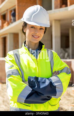 Architetta sorridente in giacca ad alta visibilità in piedi Foto Stock