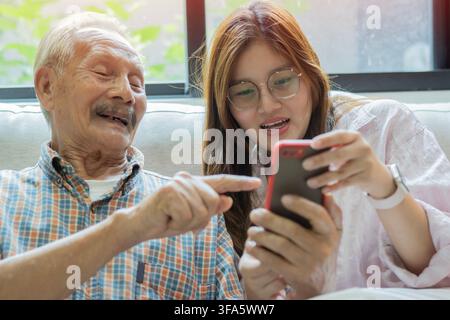 Nonno e nipote felici si divertono con lo smartphone, sorridono a un video divertente, giocano a un gioco mobile. Foto Stock