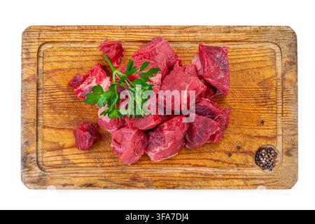 Cubetti di carne rossa cruda e un rametto di prezzemolo sono posati su un tagliere di legno. Un piccolo buco nel tagliere contiene grani di pepe nero. Carne cruda Bsip 016952 160 Foto Stock