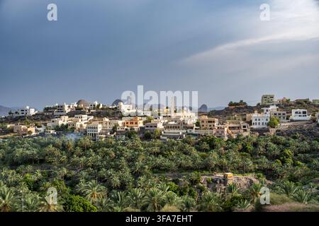 Villaggio tradizionale omanita circondato da una lussureggiante oasi di palme da dattero e montagne Foto Stock