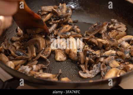 Prima vista di funghi affettati saltati in padella con una spatola di legno. Foto Stock