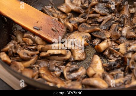 Un primo piano mostra funghi affettati saltati in padella con una spatola di legno. Foto Stock
