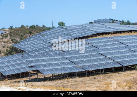 File di pannelli fotovoltaici sono installati su una collina baciata dal sole, catturando energia solare in un ambiente rurale Foto Stock