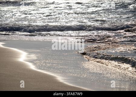 Spiaggia di Ayfilon. Dipkarpaz. Cipro del Nord. La luce dorata del sole si riflette sulle dolci onde del mare che si infrangono su una costa sabbiosa durante il tramonto Foto Stock