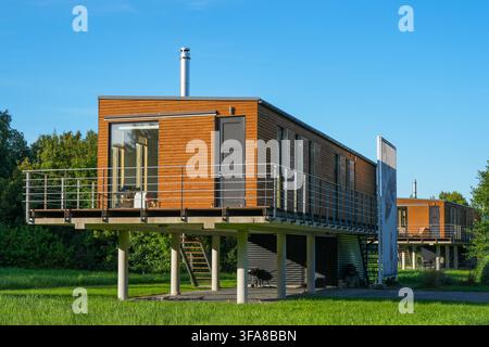 Pavilosta, Lettonia - 09 agosto 2026: Case residenziali moderne rivestite in legno su pilastri di cemento con balconi e grandi finestre in un paesaggio verde Foto Stock