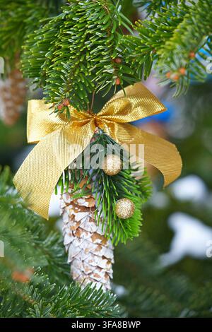 Decorazione per albero di Natale ornata, all'aperto, con pigna, fiocco di nastro dorato, ornamenti dorati, da una prospettiva ravvicinata, con accenti verdi e dorati Foto Stock