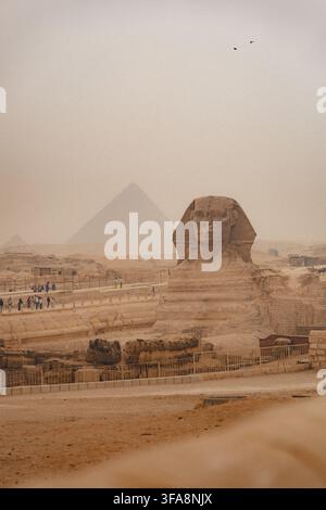 Sphynx sullo sfondo delle Grandi Piramidi Egiziane. Africa, altopiano di Giza. Una tempesta di sabbia nell'aria che conferisce un aspetto arancione al cielo. Foto Stock