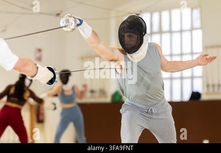 Un gruppo di recinti si allena in duelli e fa uscire i colpi sui cuscini in palestra Foto Stock