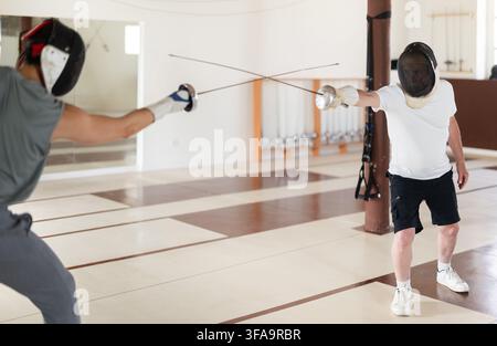 Un gruppo di recinti si allena in duelli e fa uscire i colpi sui cuscini in palestra Foto Stock