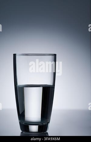 un bicchiere alto e trasparente riempito a metà con acqua potabile su uno sfondo luminoso bianco chiaro e con vignetta scura Foto Stock