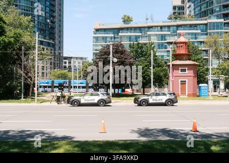 Toronto, Canada - 20 giugno 2026: veicoli della polizia e faro storico nel centro di Toronto in una giornata estiva soleggiata Foto Stock