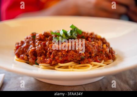 Una vista ravvicinata di un piatto di spaghetti appena servito, ricoperto da una generosa porzione di ricca e densa salsa bolognese e guarnito con trito Foto Stock