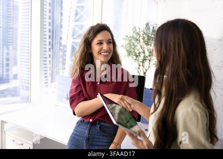 Due donne d'affari sorridenti che si stringono la mano in un ufficio di coworking Foto Stock