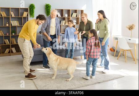 Famiglia multigenerazionale felice che gioca con un labrador in un soggiorno accogliente Foto Stock