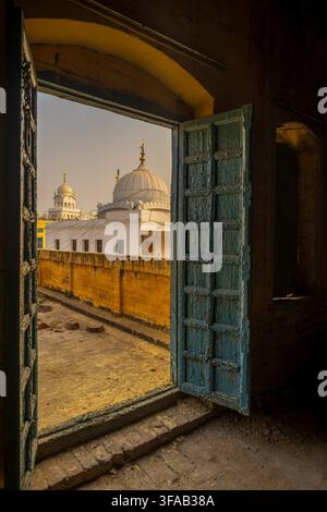 Vista del Gurudwara Bal Lila Sahib vista attraverso una porta di legno blu aperta e consumata da una terrazza sul tetto a Nankana Sahib, Punjab, Pakistan. Foto Stock