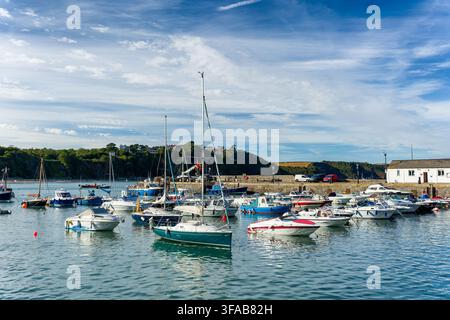 Barche a vela e motoscafi ormeggiati che galleggiano sull'acqua calma del mare all'interno del porto di Tenby, scogliere verdi e muro di pietra del molo sullo sfondo, Pembrokeshire, Sud Foto Stock