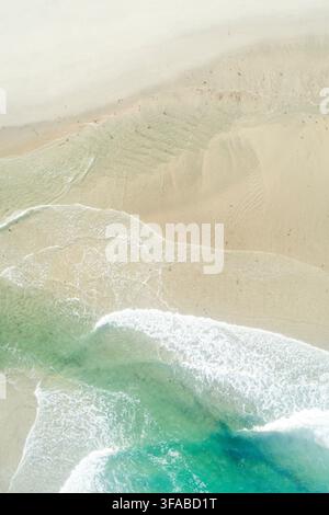 Vista aerea dall'alto di dolci onde turchesi dell'oceano che si infrangono su una spiaggia di sabbia incontaminata Foto Stock