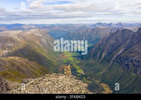 Vista aerea del picco montuoso Kongen con un cumulo di pietre in primo piano che si affaccia sulla valle verdeggiante e sui ripidi pendii rocciosi di Andalsnes, M Foto Stock