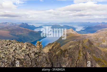 Vista aerea del picco del monte Kongen che si affaccia sul Romsdalsfjorden con terreno roccioso impervio, acqua blu profonda e montagne lontane ad Andalsnes, Møre Foto Stock