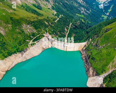 Vista aerea della diga dello Stausee Mooserboden con acqua del bacino turchese, circondata da ripide montagne alpine verdi e strade tortuose a Kaprun, Salisburgo Foto Stock